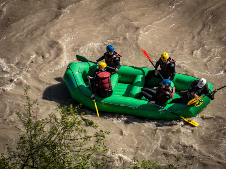 un raft vert sur une rivière de couleur marron à cause de la pluie.